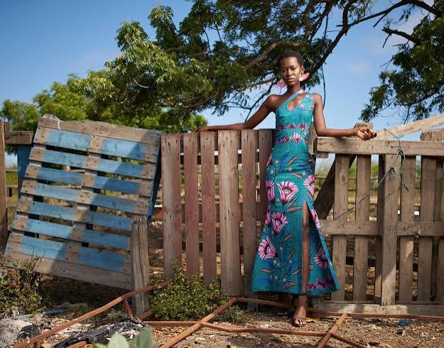 A woman wearing a custom teal floral gown standing by a wooden fence