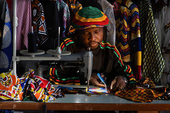 A tailor concentrating at his sewing machine surrounded by wax print fabrics