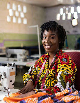 A smiling tailor at her sewing machine with bright wax fabric